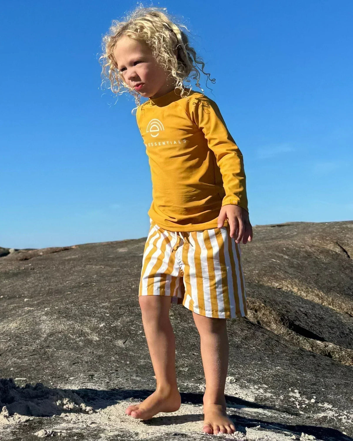 child with yellow swim t-shirt and striped swim shorts standing on dunes
