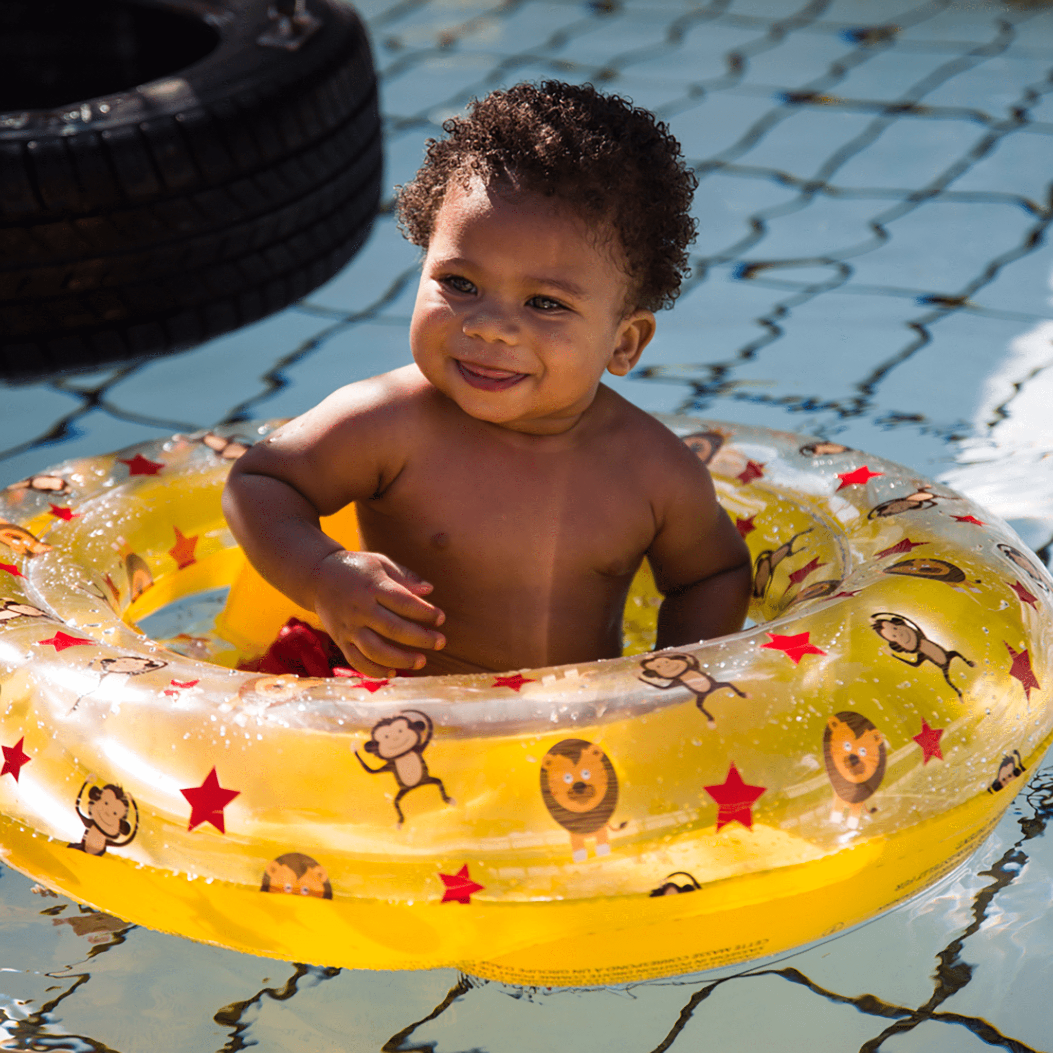 Child in a yellow inflatable ring with animal patterns in a pool.