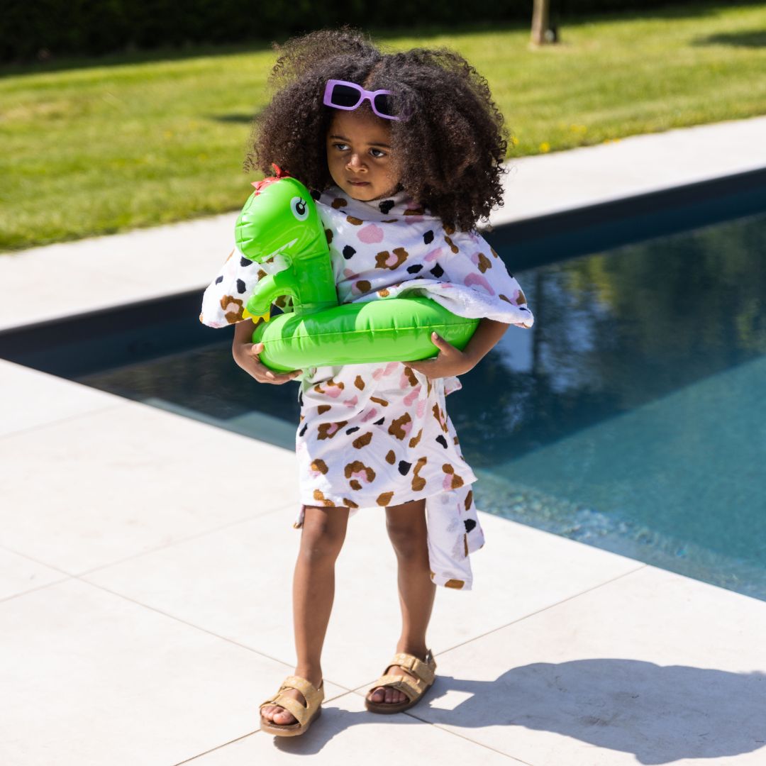 Child holding a green inflatable dinosaur by a pool